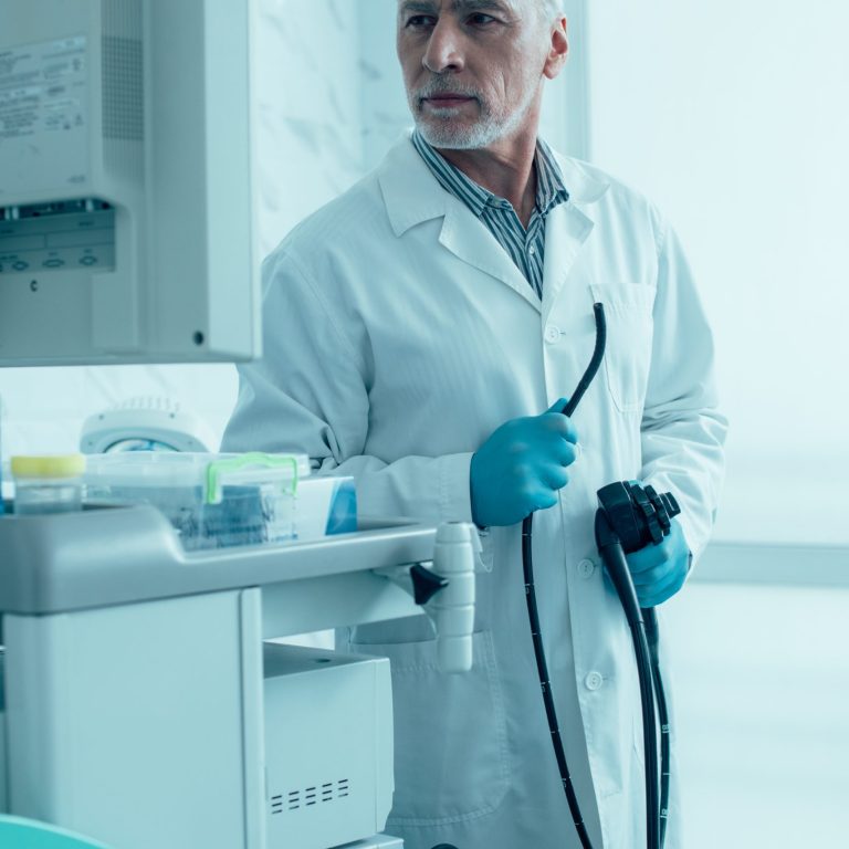Calm mature doctor looking at the screen and holding an endoscope stock photo